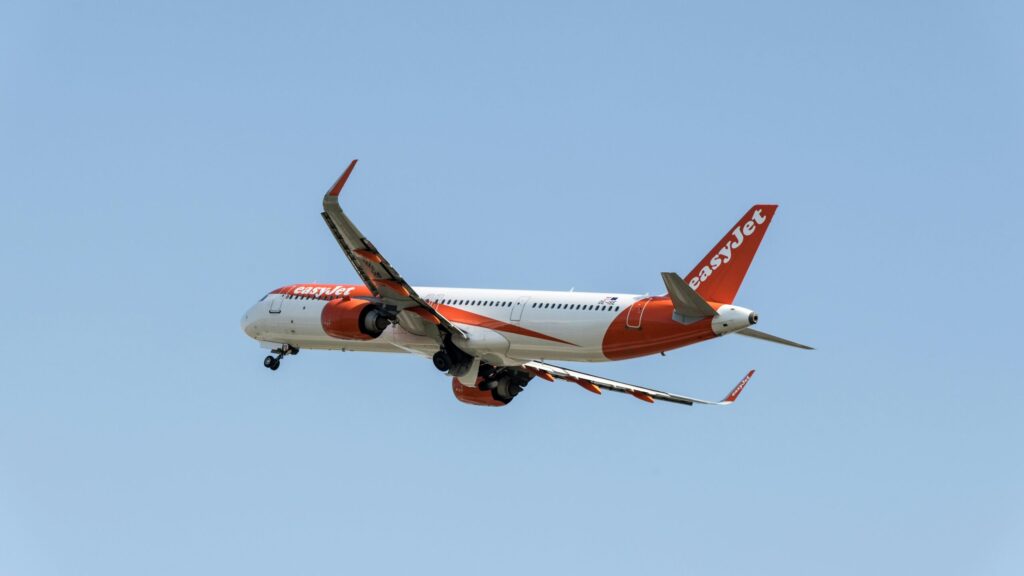 EasyJet airplane captured mid-flight above Prague with a clear blue sky background.